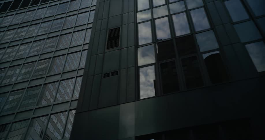 The reflections of nearby buildings and the sky shine on the surface of a tall downtown building
