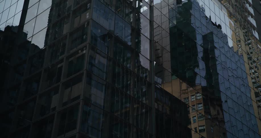 The reflections of nearby buildings shine on the surface of a tall downtown building