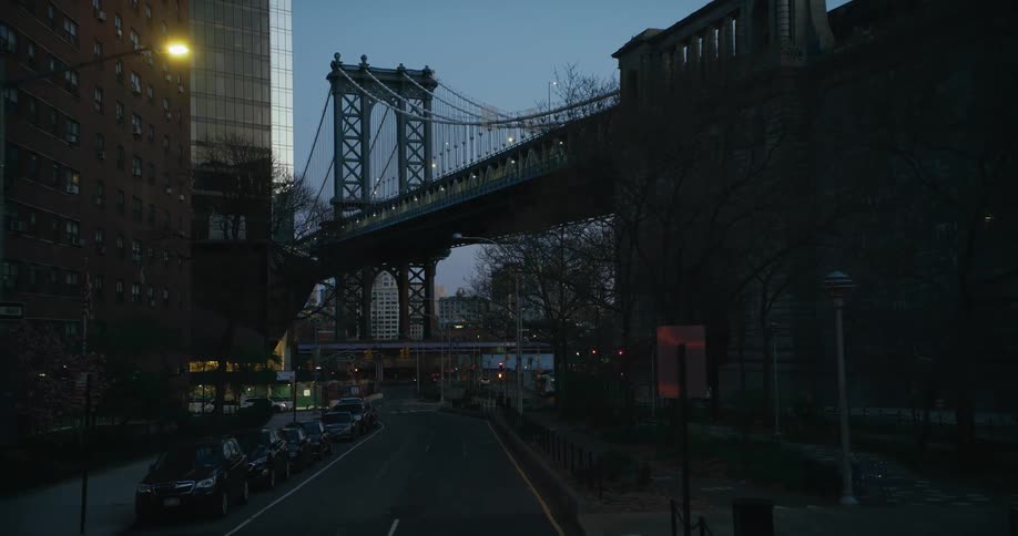 Streetlights shine over street crossing under large suspension bridge and small bridge