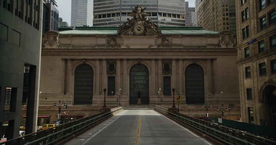 A one way bridge leads to a building surrounded by tall skyscrapers