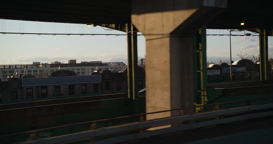 A vehicle drives on a multi level bridge past a city neighborhood