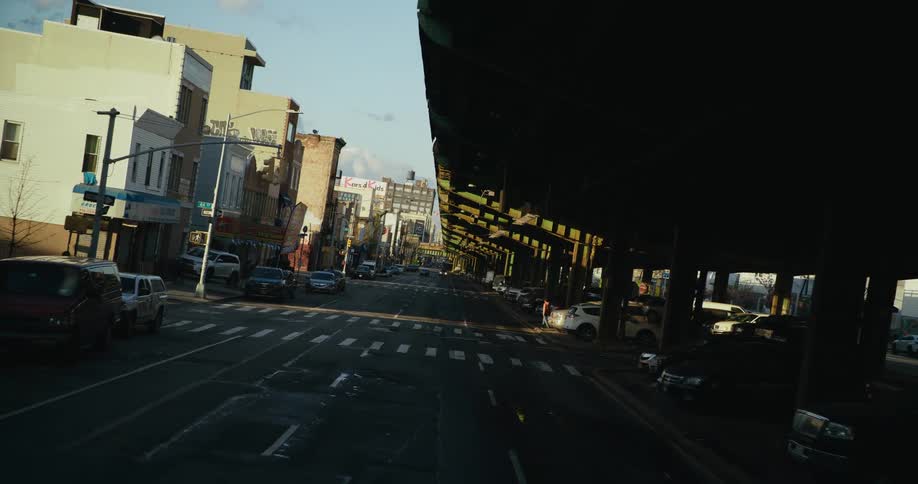 A man walks across the street with his dog heading toward the parked cars under the elevated highway ramp