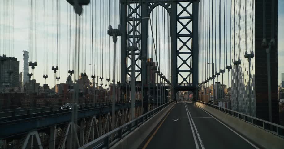 Vehicle crosses bridge with tower and skyscrapers in the background