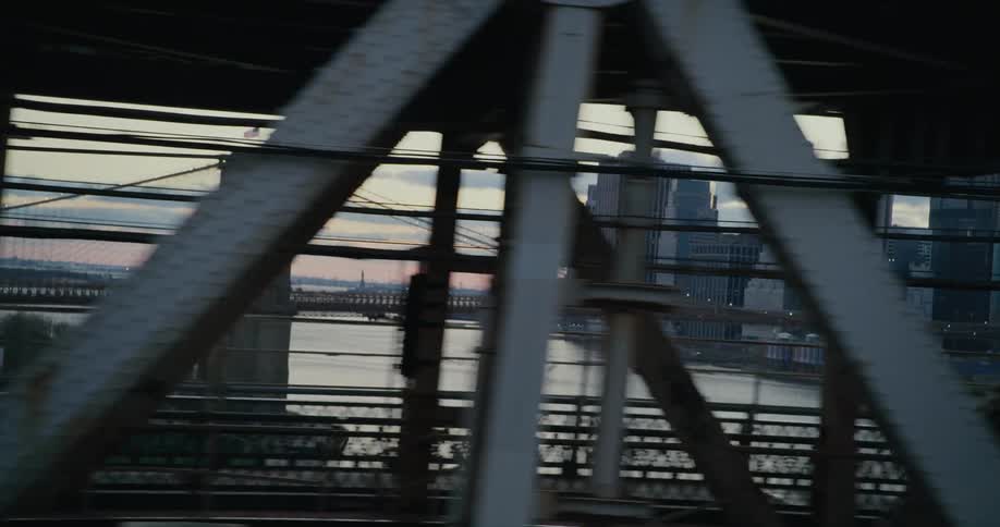A car travels across a bridge towards the city with a train heading in the opposite direction