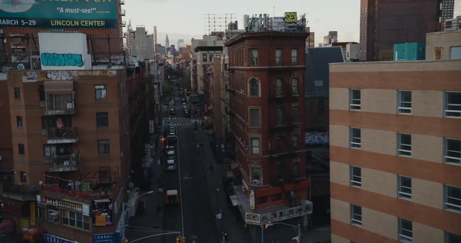 Vehicles drive past apartment buildings in a dense city neighborhood