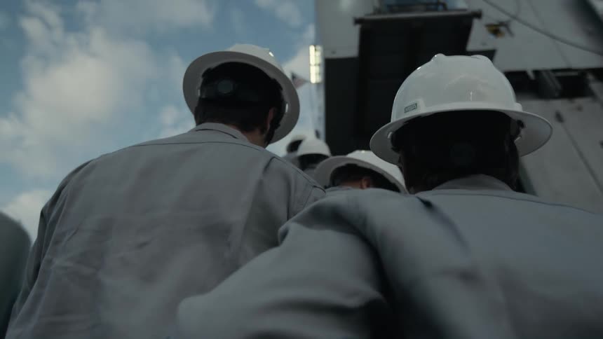 Workers wearing hardhats climb stairs of building situated near storage tanks