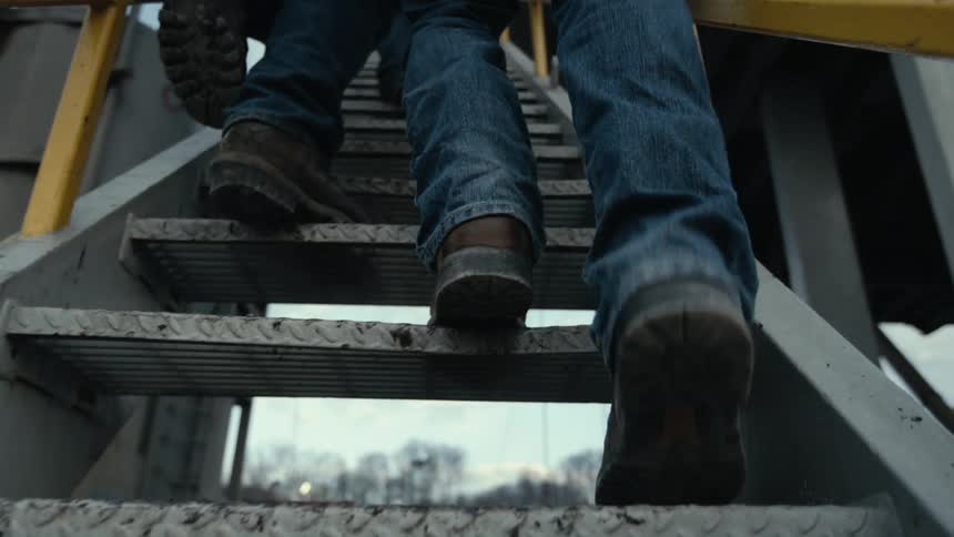 Two men in work boots walk up the steps at a refinery