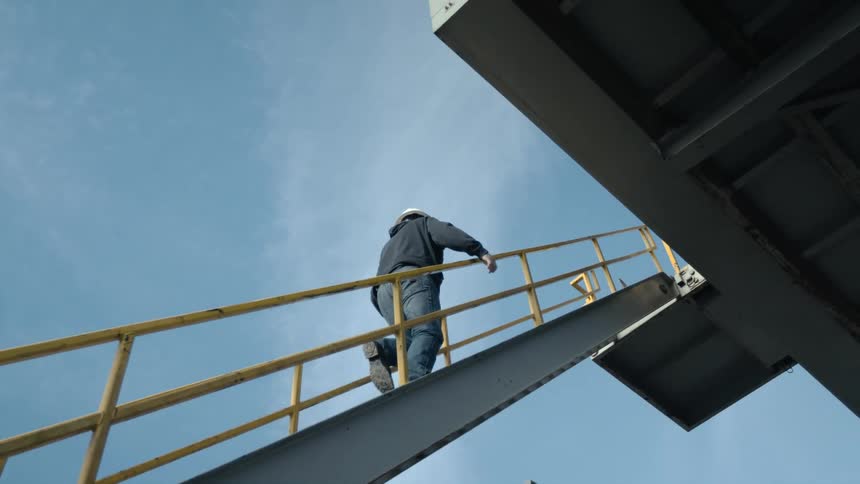 Worker wearing hard hat climbs staircase attached to factory building