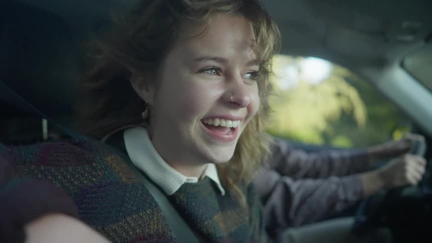 Woman with wavyh hair piercing sitting next to man driving car laughs