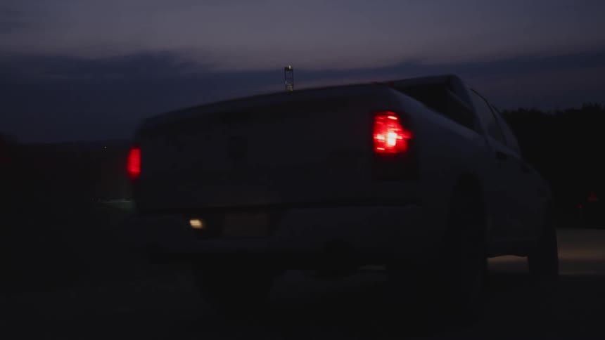 Vehicles including an utility truck drive along road toward plant at night