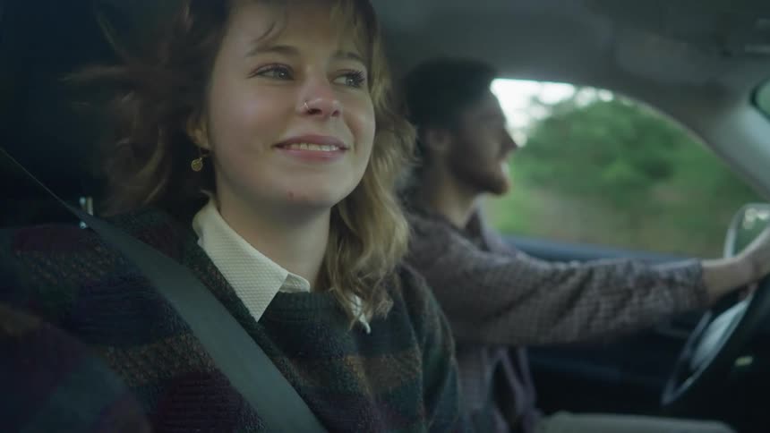 A woman rides as a passenger in a car and smiles while looking out of the window