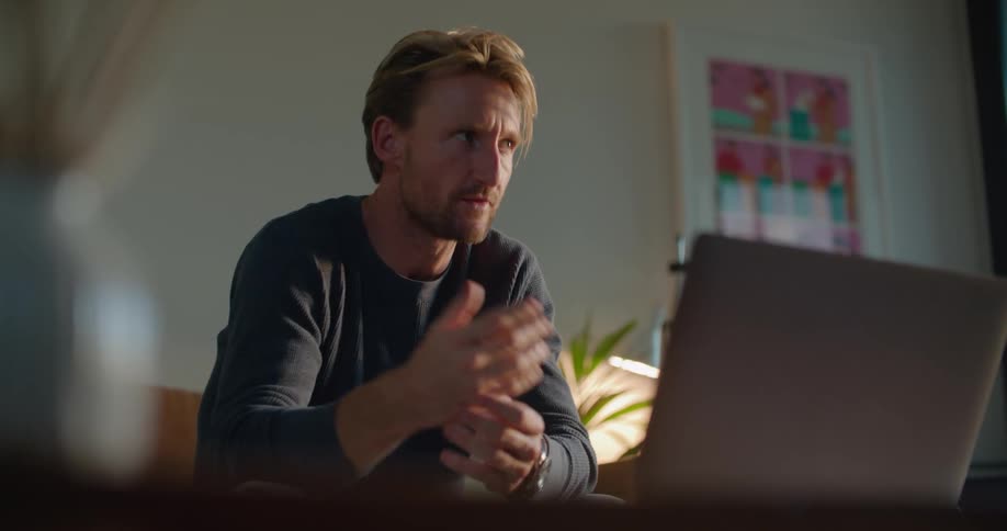 Man sits on couch answering questionsvia a video conference on a laptop