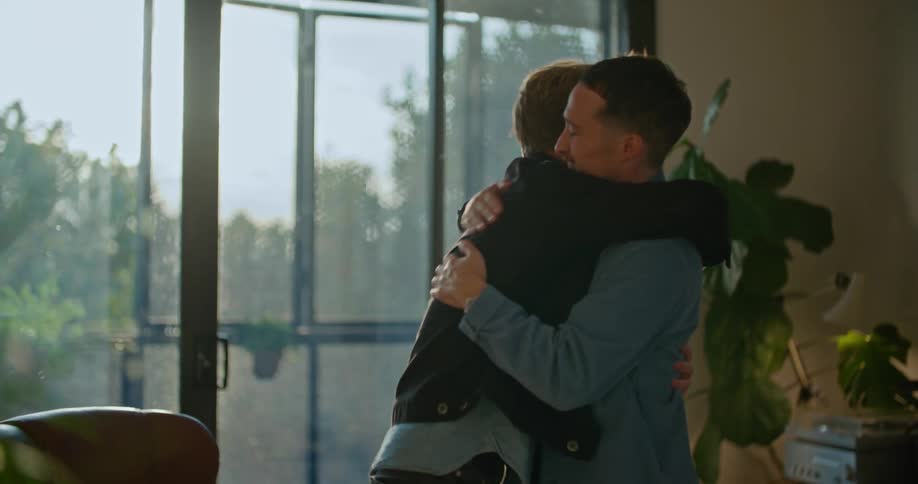 Two men stand up from their chairs and give each other a hug before one walks away