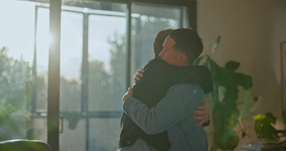 Two men are sitting in chairs and they stand and hug and one man walks away