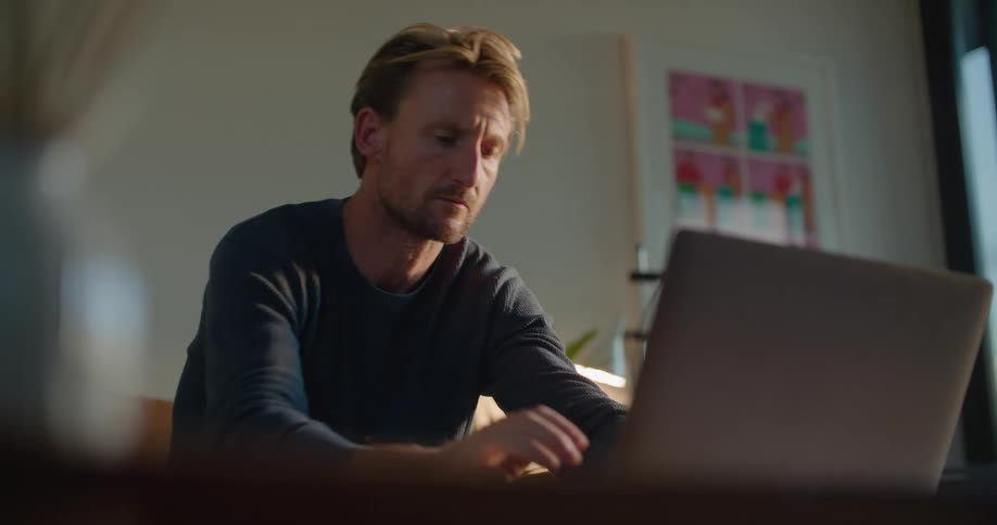 A man strokes his chin and clasps his hands while thinking then begins to type
