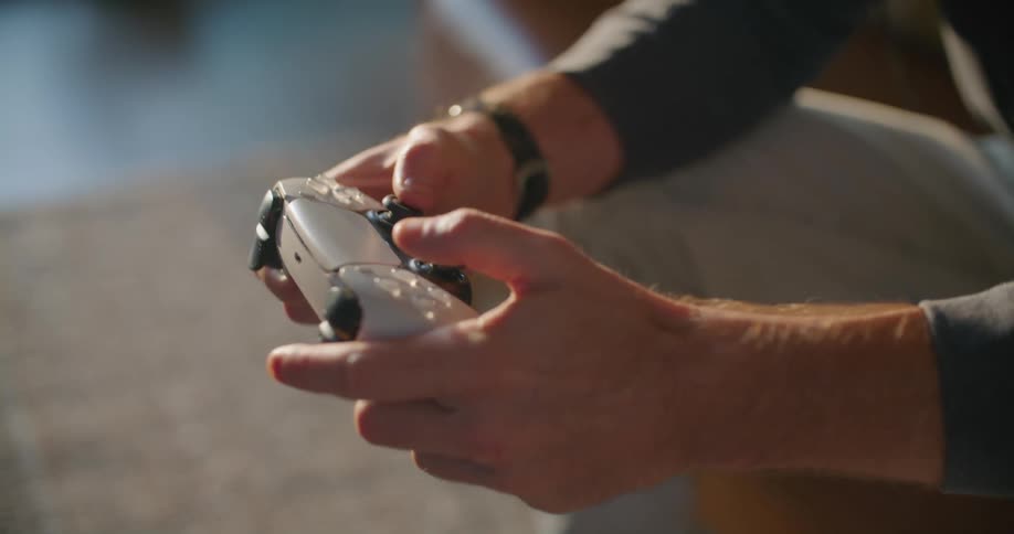 A man who is seated is rapidly pressing buttons on a wireless video game controller