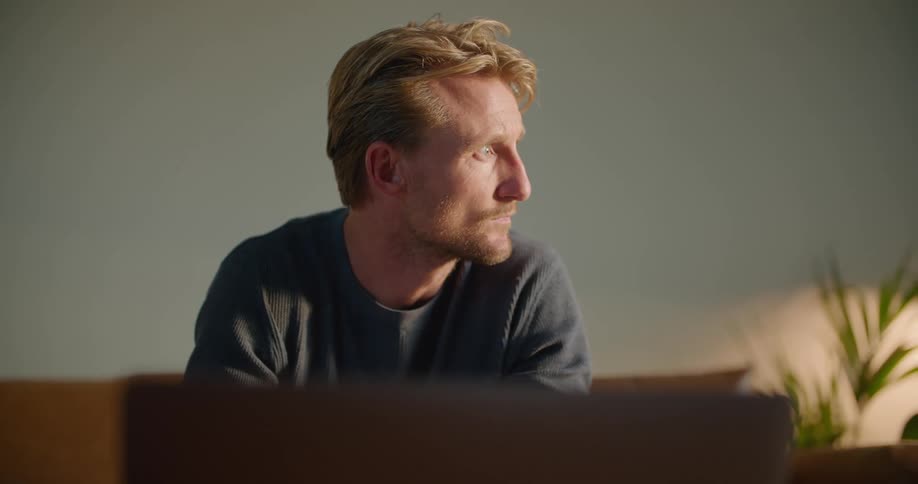 A man is sitting on a couch and typing on a laptop
