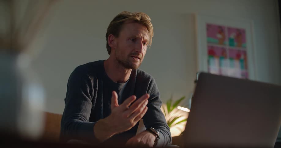 Man sits on couch holding discussion via laptop video call