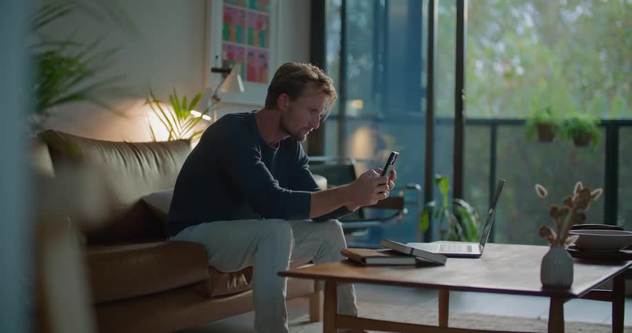 Man sits on sofa working with smartphone and laptop
