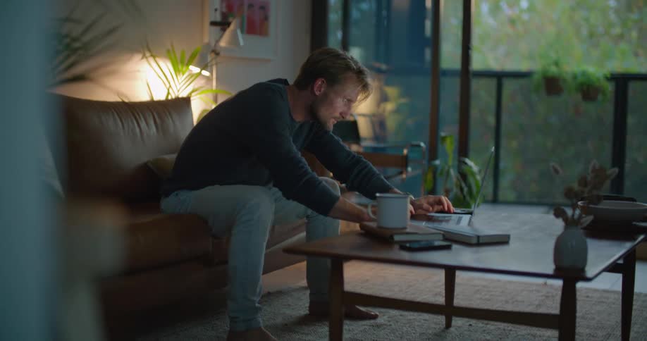 A man is walking in his living room and sitting on a couch