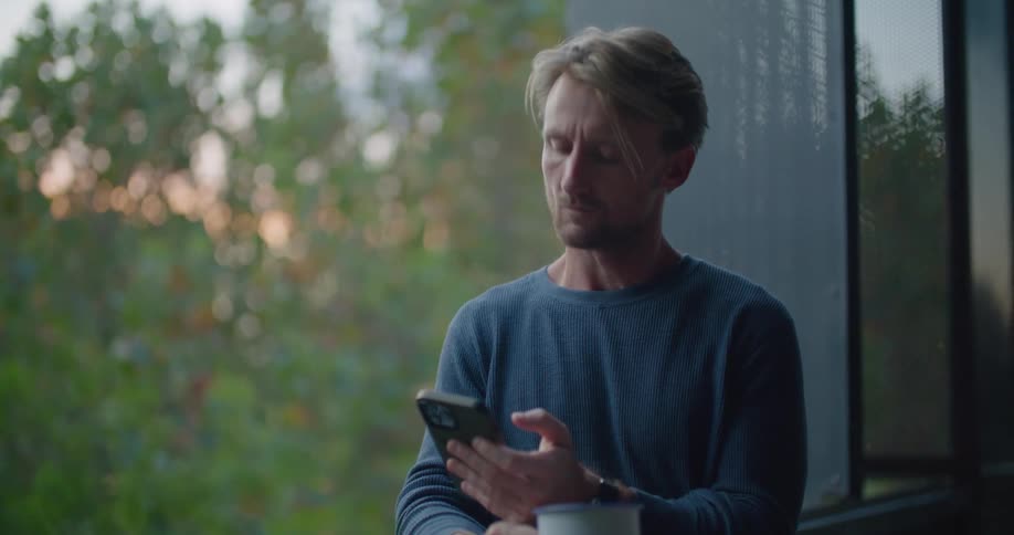 A man is texting on his cell phone and drinking coffee