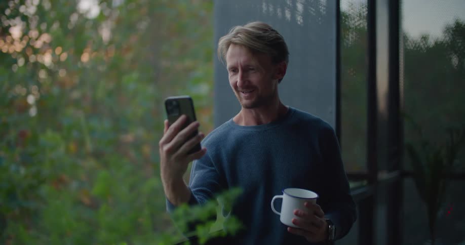 A man is drinking coffee and texting on a cell phone