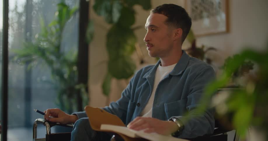 Two men are sitting in chairs talking and one man has a book open and a pen in his hand