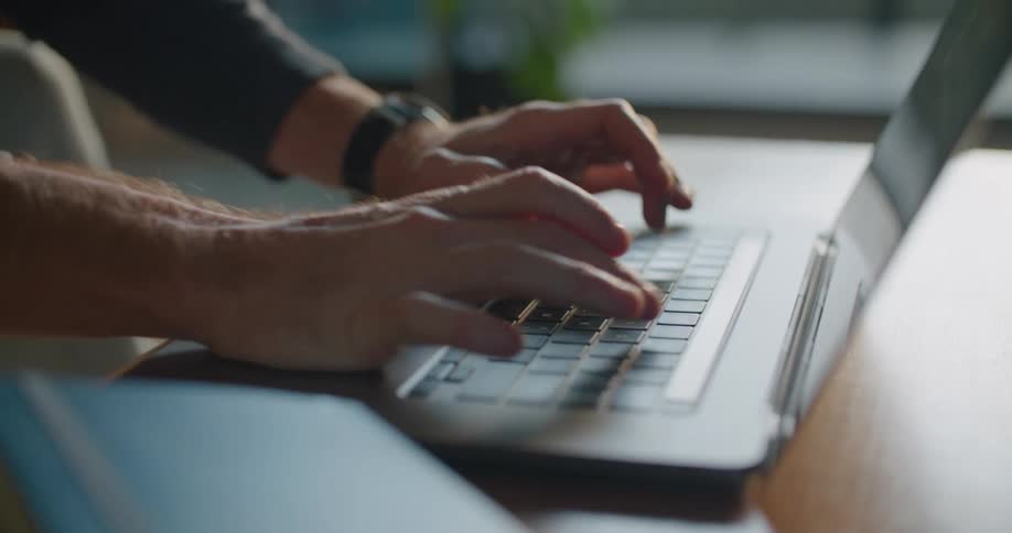 A man types on a laptop while sitting indoors during the day