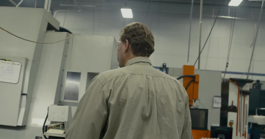 A man walks past cubicles and toward machinery in a warehouse