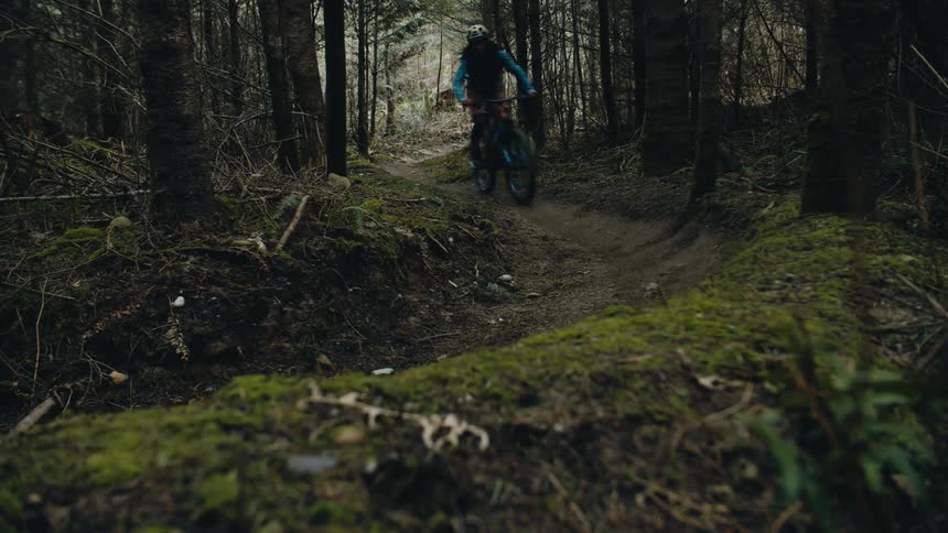 A woman wearing a helmet is riding a bike on a trail in the woods