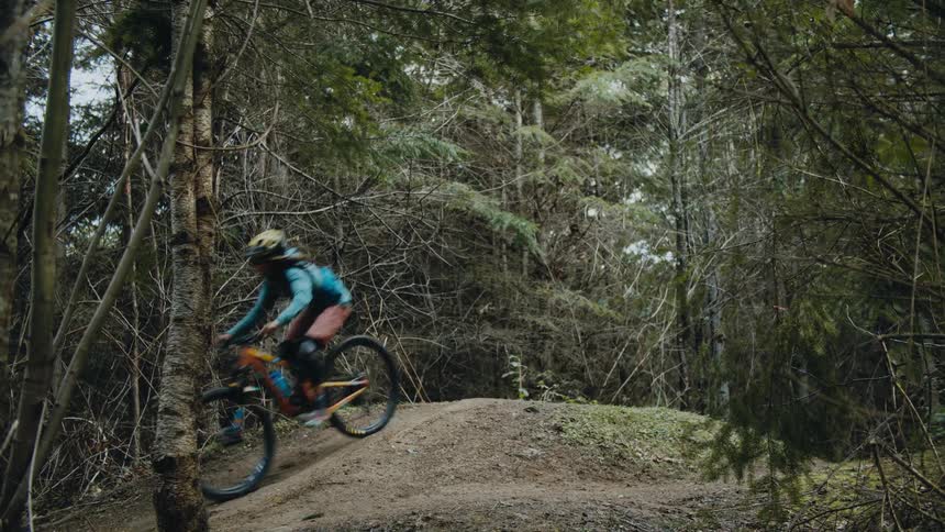 Cyclists riding dirt bike takes jump on mound in forest