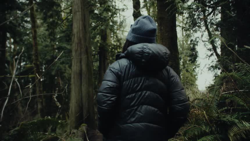 A woman walks through a forest with her hands in her coat pockets