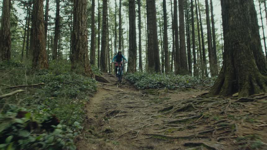 A woman driving a mountain bike on a trail through the forest downhill