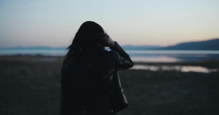 A woman runs her hand through her hair while walking on the beach toward the ocean
