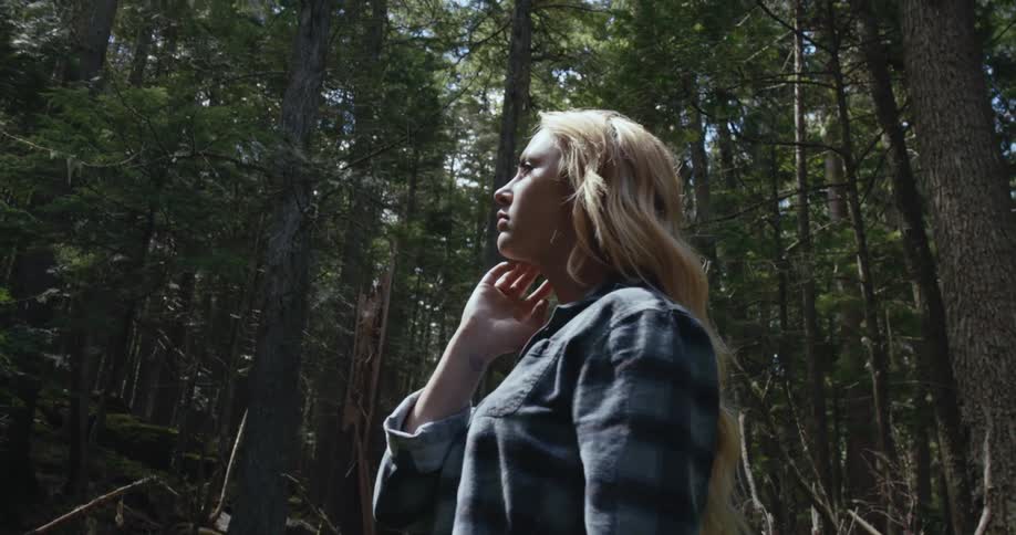 Blonde woman stands in conifer forest on sunny day