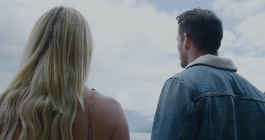 Young couple touch foreheads while holding hands in front of a lake in the mountains