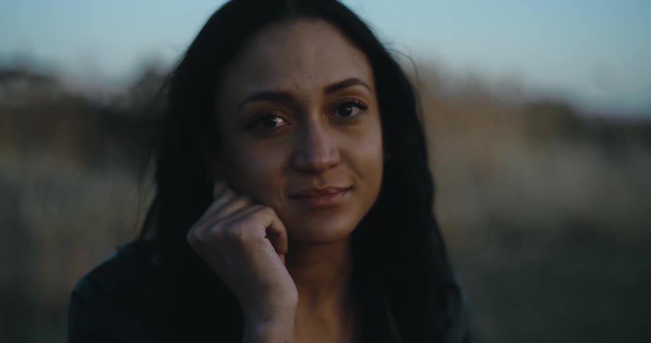 A woman is smiling and standing outdoors at midday