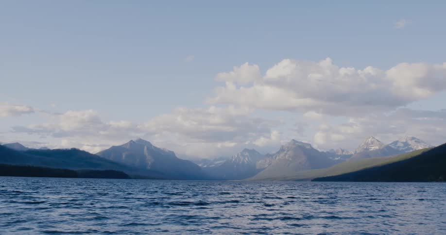 Waves flow across surface of water moving away from mountains on shore
