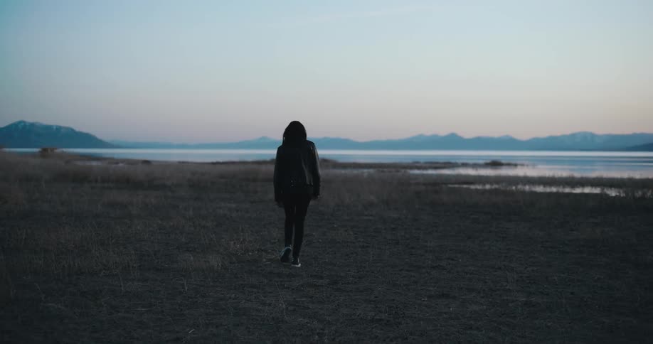 Young woman walking towards the shoreline of a beach at evening