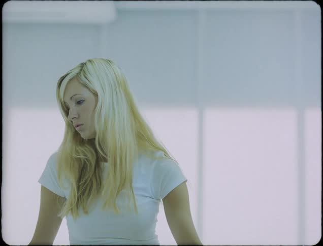 A teenage girl with long blond hair is standing still and looking to her side