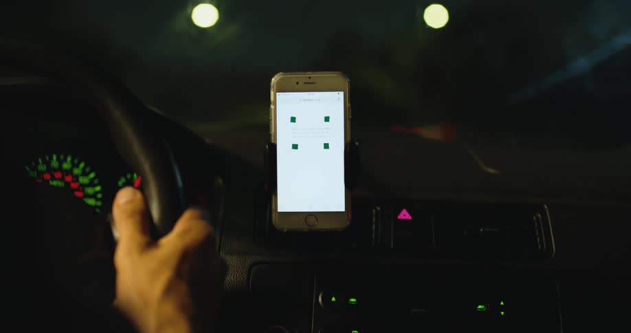 Man drives car at night using with his smartphone sitting in a hands free holder