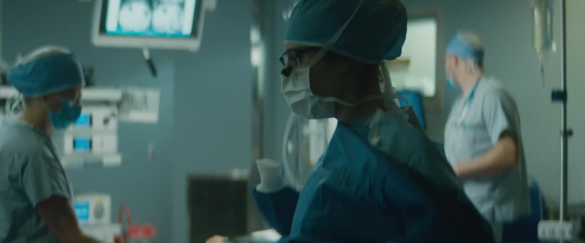 A nurse holds up a surgeons gown for her to put on in an operating room