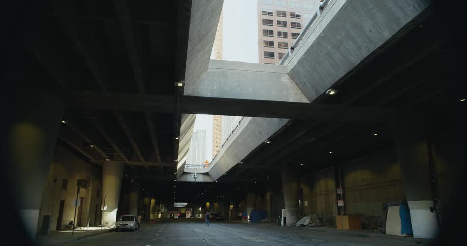 A car is parked in an indoor parking area and people are in the middle of the road and buildings can be seen through the roof