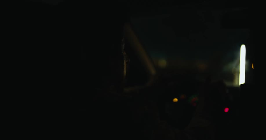 The faint silhouette of a person can be seen as they drive a vehicle in the dark of night
