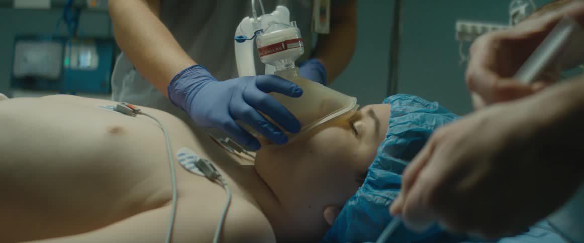 Medical person injects medication into iv of patient lying on bed being given oxygen