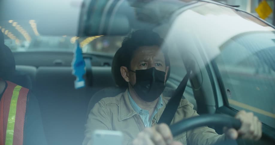 A driver wearing a face mask looks anxious as he travels on a city street
