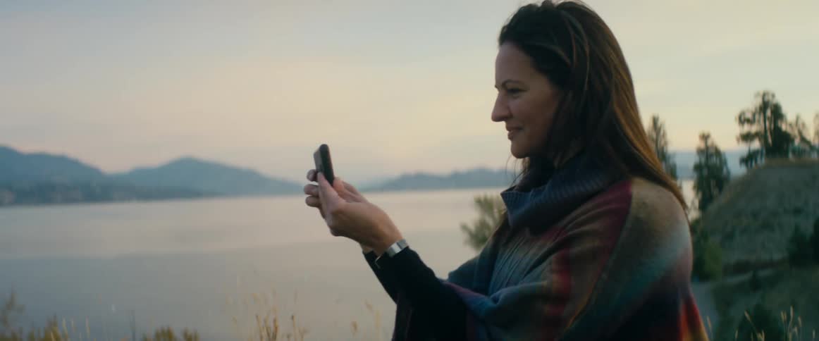A woman takes a photo with her phone by the water