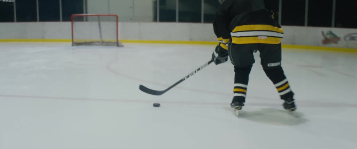 A person skating very quickly uses their hockey stick to shoot the puck into the net
