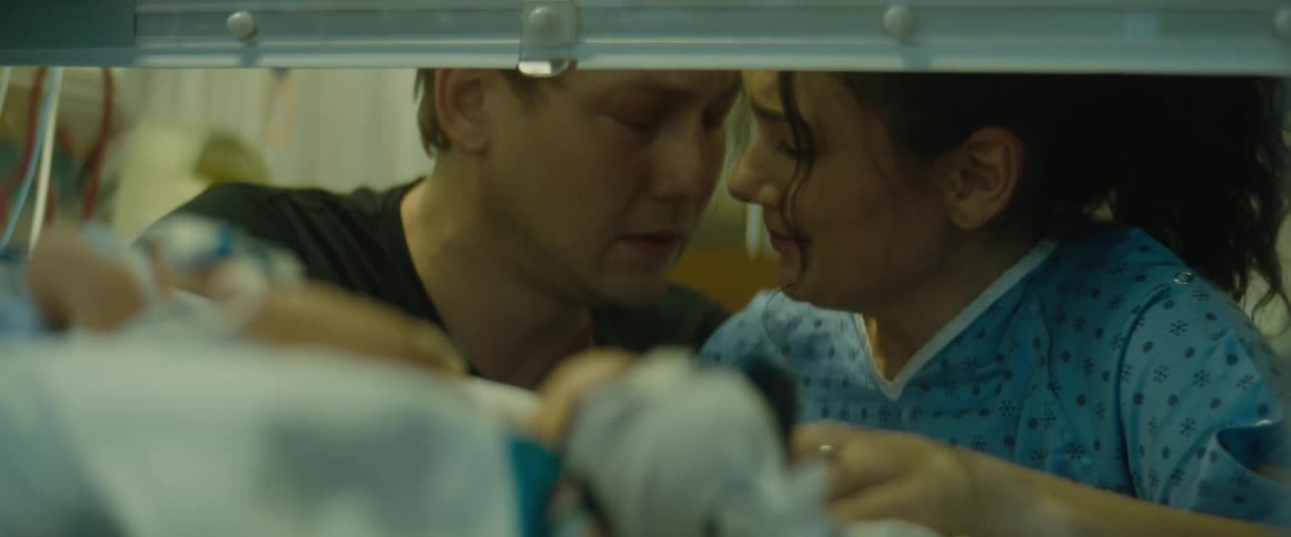 A man and woman comfort each other as they visit their newborn in a nicu incubator