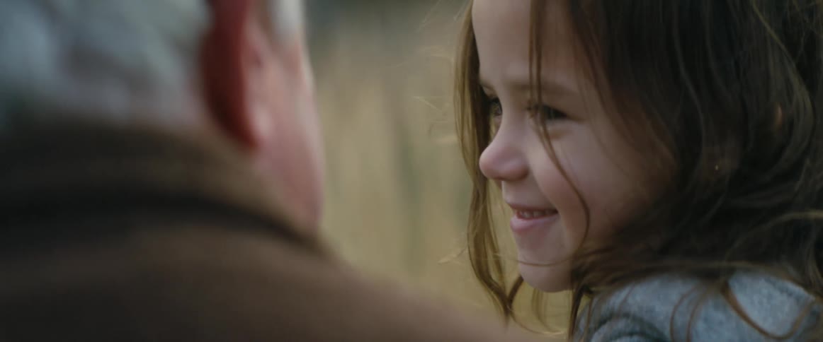 A young girl smiles as she looks over at her grandfather nearby